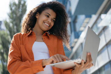 African American business woman using laptop computer, typing on keyboard, searching information on website. Successful business concept. Smiling hipster girl working freelance project remotely 