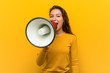© Asier - Young european woman holding a megaphone shouting excited to front.