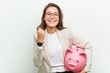 © Asier - Young european business woman holding a piggy bank cheering carefree and excited. Victory concept.