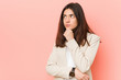 © Asier - Young brunette business woman against a pink background looking sideways with doubtful and skeptical expression.