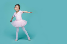 Beautiful Smiling Asian Little Girl In A Pink Suit Is Dancing A Ballet At School, Empty Space In Studio Shot Isolated On Colorful Blue Background