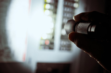 photo during a power outage with silhouette of hand holding a flashlight aimed at a fuse box