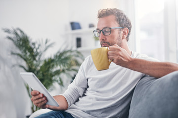 Wall Mural - Man holding tablet, surfing online and drinking coffee.