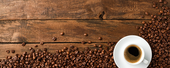 Wall Mural - Black coffee cup with beans on retro wooden background with copyspace. Top view. Banner