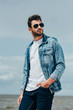 handsome man in denim jacket and sunglasses looking away