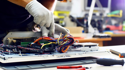 Wall Mural - Technician works in service center. Repairman detaches power supply repairs computer monoblock in workshop. He disconnects wires, takes out and puts detail on table, continues to diagnose monitor.