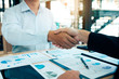 © wutzkoh - Entrepreneurs collaboration deal shaking hands in a modern office and financial paper graph on desk.