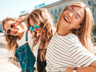 Portrait of three young beautiful smiling hipster girls in trendy summer clothes. Sexy carefree women posing on the street background.Positive models having fun in sunglasses.Hugging