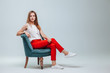© Smeilov - Girl in red pants sitting in a chair on a light gray background