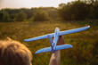 Cute white kid playing happily outdoor with big toy plane during gold sunset time in summer landscape. Horizontal color photography.