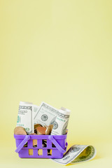 Wall Mural - Shopping basket with coins and dollar bills on yellow background. Space for text. Close up. Business concept.