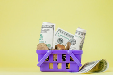 Wall Mural - Shopping basket with coins and dollar bills on yellow background. Space for text. Close up. Business concept.