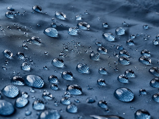 Rain water droplets on blue fiber waterproof fabric. Blue background.