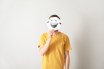 Sticker - Man hiding face behind sheet of paper with drawn emoticon on grey background