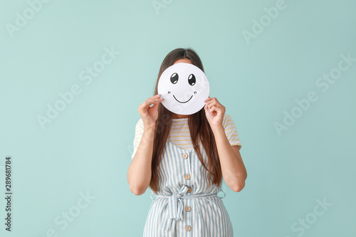Fotomural Woman hiding face behind sheet of paper with drawn emoticon on color background