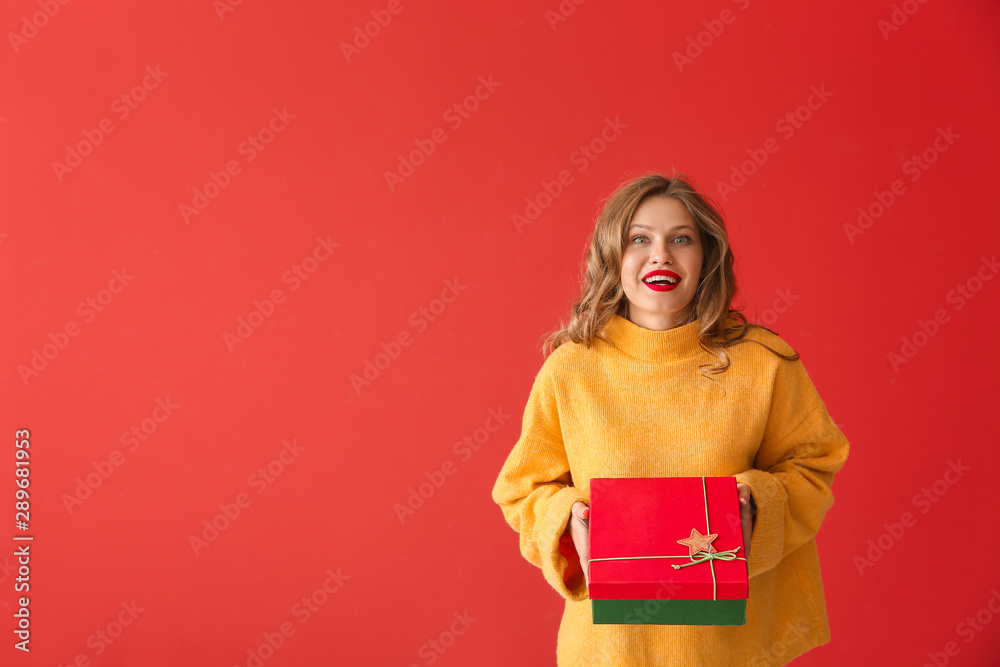 Happy young woman with Christmas gift on color background