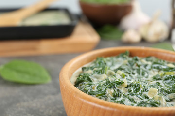 Tasty spinach dip in wooden bowl on grey table, closeup