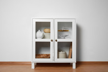 Wooden Cabinet With Kitchenware Near White Wall