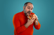 © nazarovsergey - Close-up portrait of a middle-aged man with beard, dressed in a red turtleneck, posing with burgers against a blue background. Fast food.