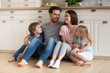 © fizkes - Happy family of four sitting on wooden floor at kitchen.
