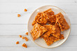 Plate of traditional peanut brittle candy pieces. Top view on a white wood background.
