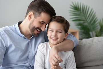 Wall Mural - Affectionate dad and child son bonding embracing sit on sofa