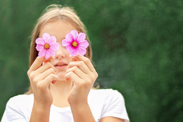 close-up portrait of teenager girl holding two pink cosmos flowers in front of her face hiding her e