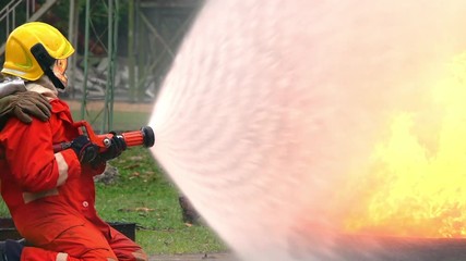 Wall Mural - HD Slow motion medium shot of firefighter in fire suit on safety rescue duty using water hoses to extinguishing a fire at a fire training class. Fireman fighting a fire inside burning premises.