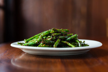 Close up side view of spicy szechuan green beans on white plate and wood surface