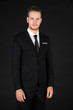 © Arunporn - Portrait of young smart and handsome business man in black suit standing on isolated black background.