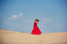 Woman In Red Dress Dancing In The Desert At Blue Sky
