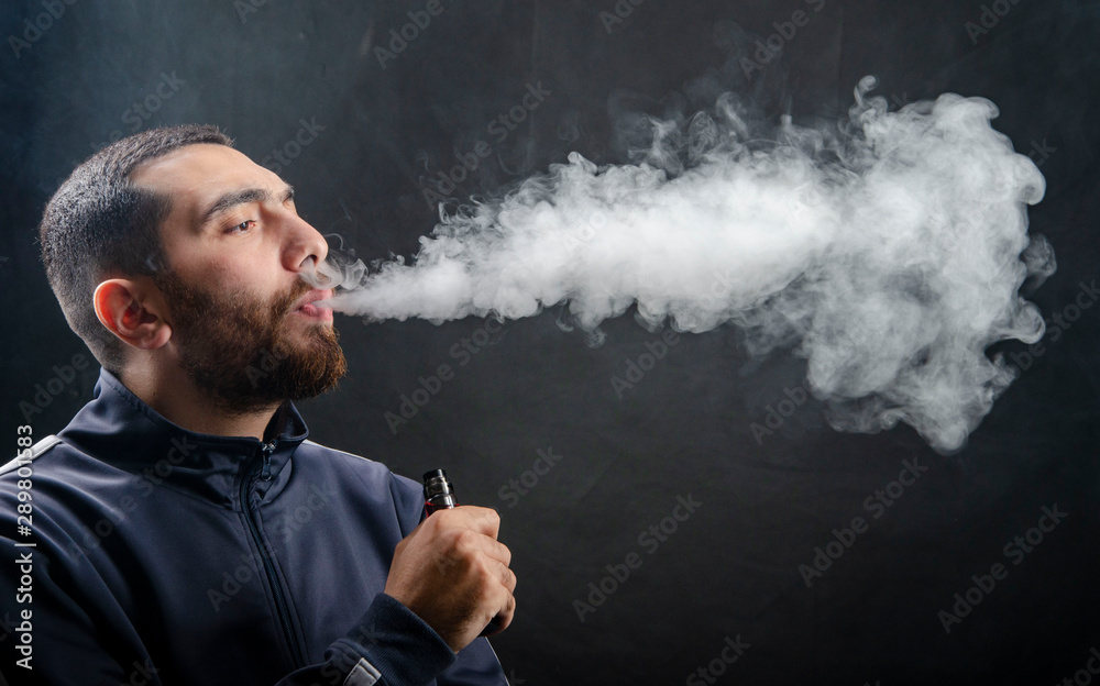 vape and smoke vape electronic e-cigarette or e-cig by a young man with  smoke clouds over a black background., obrazy, fototapety, plakaty -  BajeczneObrazy.pl