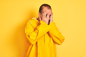 Sticker - Young man wearing rain coat standing over isolated yellow background with sad expression covering face with hands while crying. Depression concept.