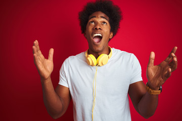 Sticker - Young african american man listening to music using headphones over isolated red background crazy and mad shouting and yelling with aggressive expression and arms raised. Frustration concept.