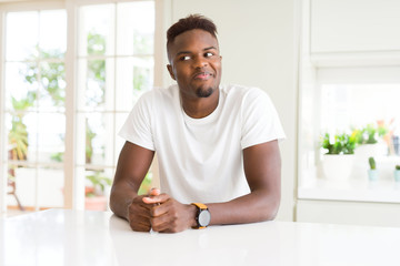 Wall Mural - Handsome african american man on white table at home smiling looking side and staring away thinking.