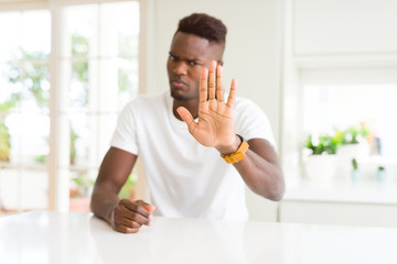 Sticker - Handsome african american man on white table at home doing stop sing with palm of the hand. Warning expression with negative and serious gesture on the face.