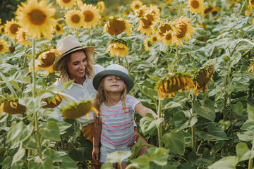 Happy mother and daughter standing in the field of sunflowers