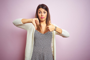 Poster - Young beautiful woman standing over pink isolated background Doing thumbs up and down, disagreement and agreement expression. Crazy conflict