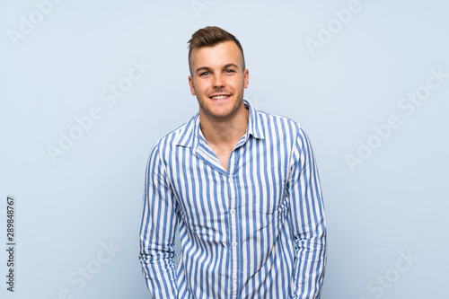 Cuadros en Lienzo Young handsome blonde man over isolated blue background laughing