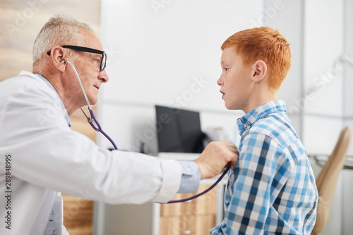 Cuadros en Lienzo Side view portrait of senior doctor using stethoscope listening to heartbeat and