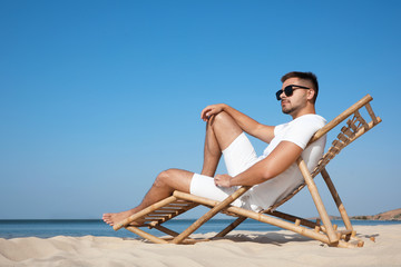 Poster - Young man relaxing in deck chair on sandy beach