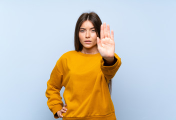 Caucasian young woman over isolated blue wall making stop gesture with her hand