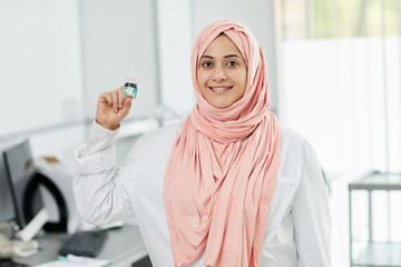 Waist up portrait of young Middle-Eastern woman working as nurse in medical clinic and smiling at camera holding bottle of pills, copy space