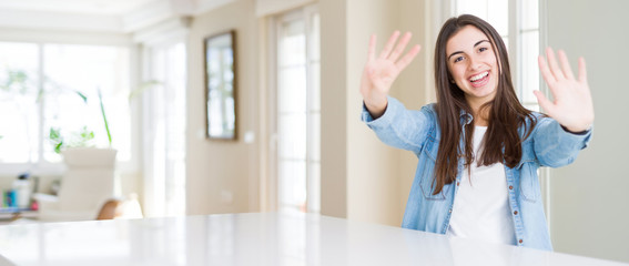 Poster - Wide angle picture of beautiful young woman sitting on white table at home showing and pointing up with fingers number nine while smiling confident and happy.