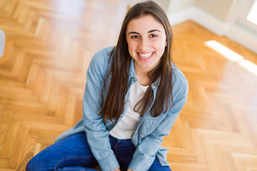 Poster - Beautiful young brunette woman smiling cheerful looking at the camera with a big smile on face sitting on the floor at home with sunlight at the background