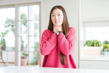 Poster - Beautiful Asian woman wearing pink sweater on white table shouting and suffocate because painful strangle. Health problem. Asphyxiate and suicide concept.