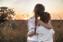 Two Little Sisters In A Field At Sunset.