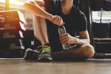 muscular caucasian young handsome man taking a break relax and drinking water while resting after workout for good healthy in fitness gym at morning, bodybuilder, lifestyle and sport exercise concept