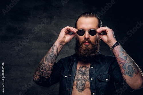 Cuadros en Lienzo Portrait of brutal bearded man with tattooes at dark photo studio