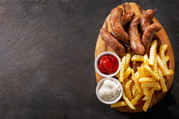 Wall Mural - fried sausages with french fries on a wooden board